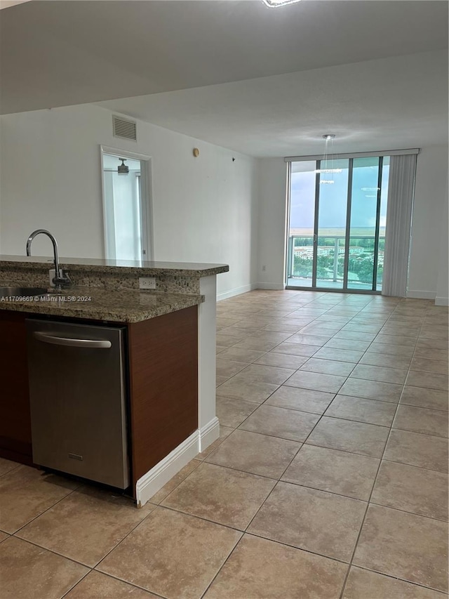 kitchen featuring expansive windows, sink, stainless steel dishwasher, dark stone countertops, and light tile patterned floors