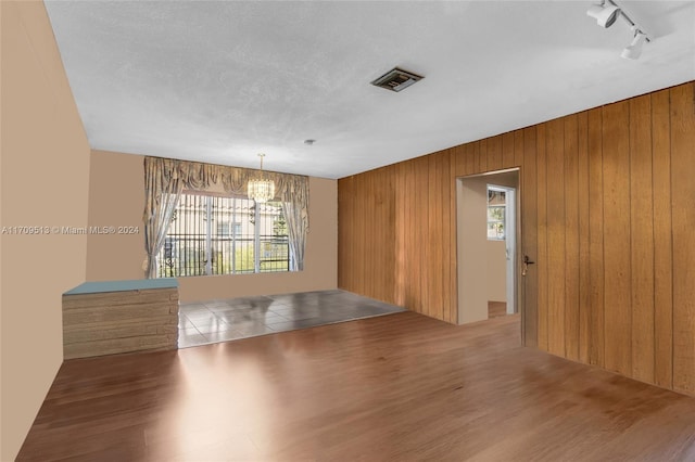 spare room with rail lighting, hardwood / wood-style flooring, a wealth of natural light, and wood walls