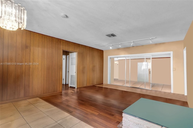 unfurnished room featuring wooden walls, an inviting chandelier, a textured ceiling, and light wood-type flooring