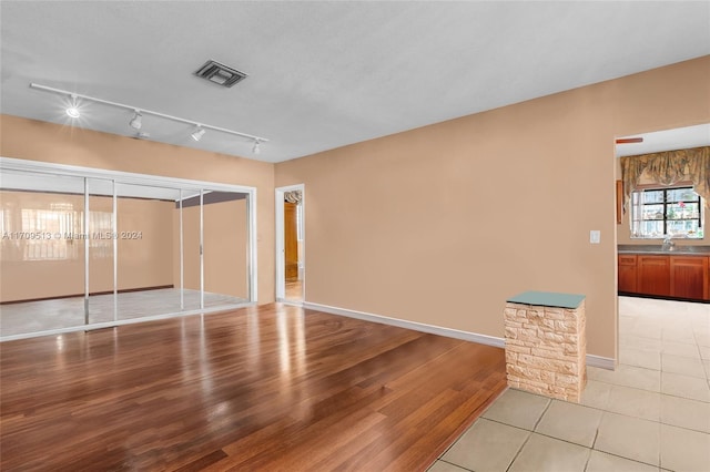 unfurnished room featuring sink, rail lighting, light hardwood / wood-style floors, and a textured ceiling