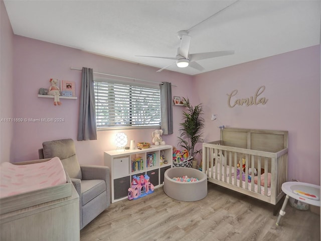 bedroom featuring ceiling fan, light hardwood / wood-style floors, and a crib