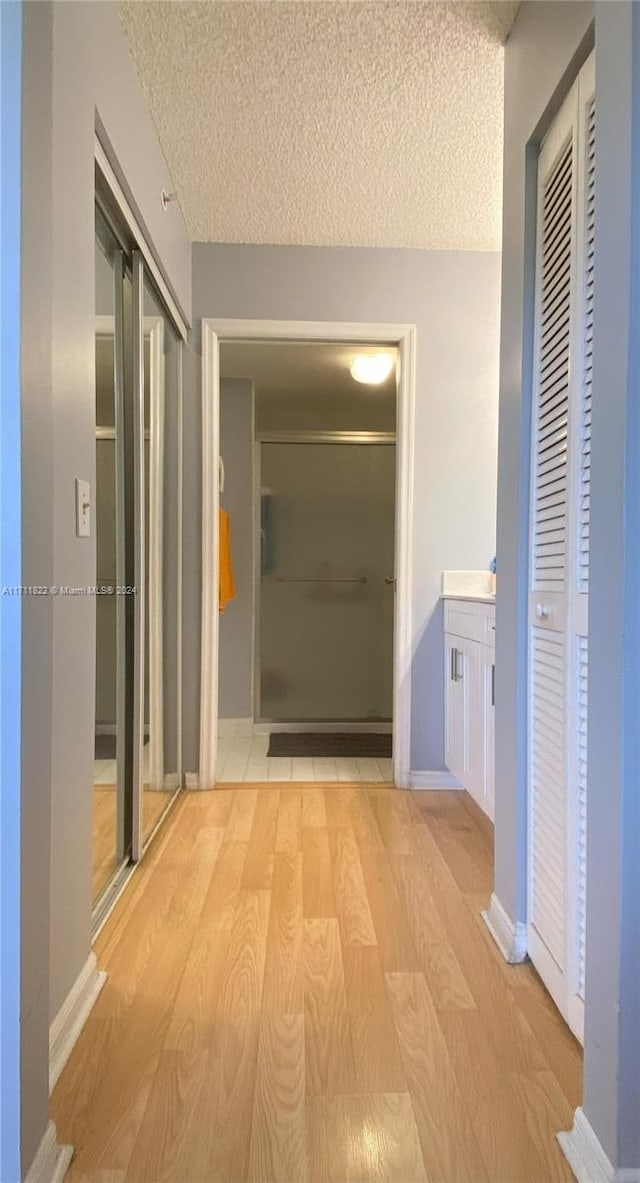 hallway with light wood-type flooring and a textured ceiling