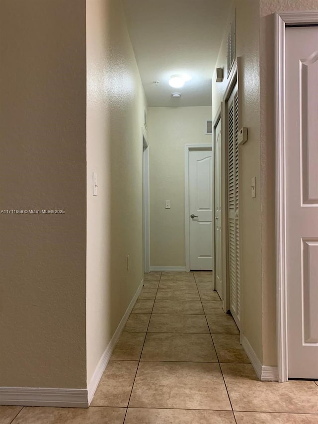 hall featuring light tile patterned floors and baseboards