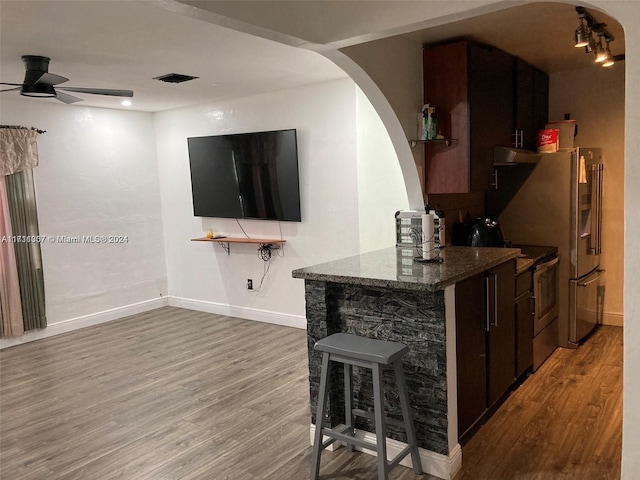 bar with dark stone counters, dark brown cabinetry, ceiling fan, wood-type flooring, and stainless steel electric range