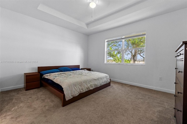 carpeted bedroom featuring ceiling fan and a tray ceiling