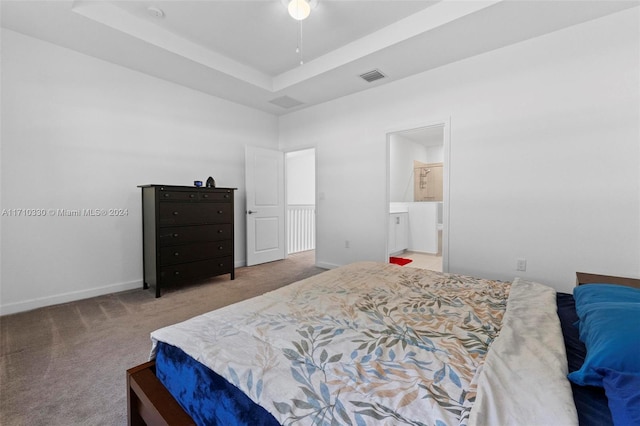 carpeted bedroom featuring ensuite bath and a raised ceiling