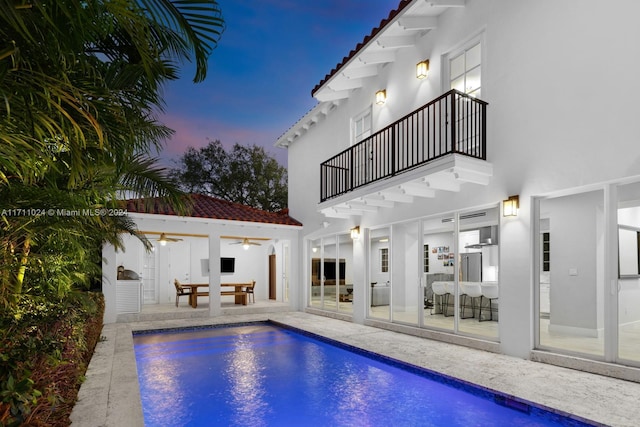 pool at dusk with ceiling fan and a patio area