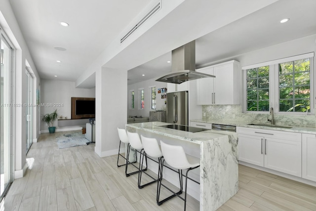 kitchen featuring island exhaust hood, high quality fridge, a kitchen island, sink, and white cabinetry