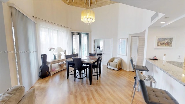 dining space featuring light hardwood / wood-style floors, a towering ceiling, and an inviting chandelier