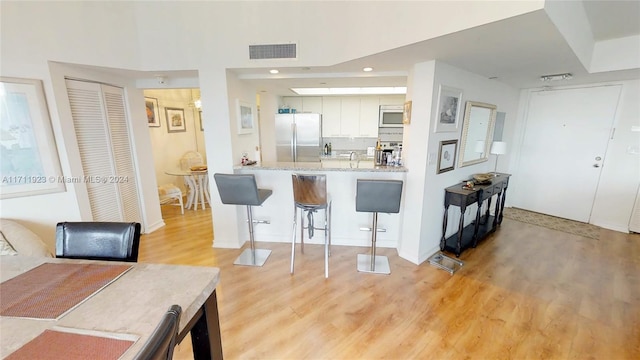 kitchen featuring a kitchen breakfast bar, kitchen peninsula, stainless steel fridge, white cabinets, and light wood-type flooring