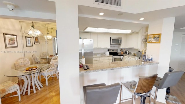 kitchen featuring kitchen peninsula, appliances with stainless steel finishes, light stone countertops, light hardwood / wood-style flooring, and hanging light fixtures