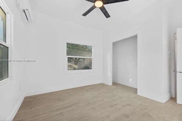 empty room with a wall mounted AC, ceiling fan, and light hardwood / wood-style floors