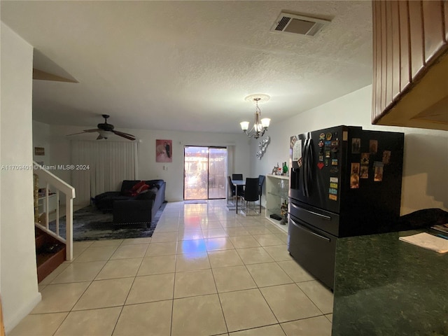 kitchen with pendant lighting, ceiling fan with notable chandelier, black refrigerator, light tile patterned floors, and a textured ceiling