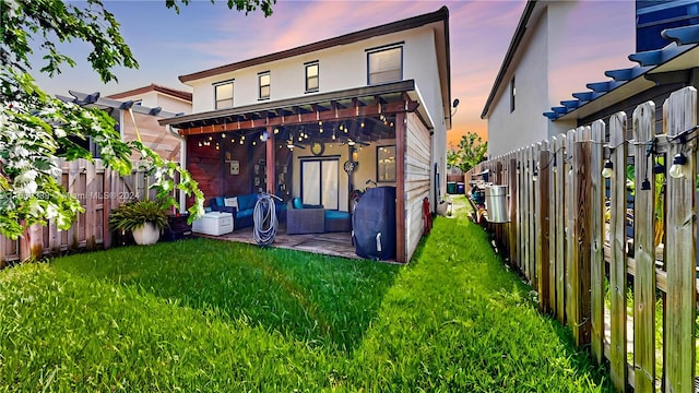 back house at dusk with an outdoor living space, a yard, and a patio area