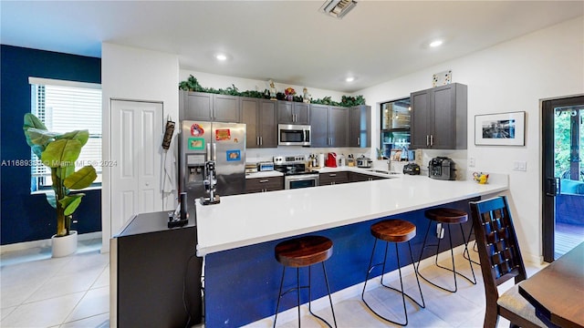 kitchen featuring kitchen peninsula, light tile patterned floors, a kitchen bar, and stainless steel appliances