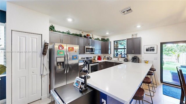 kitchen featuring a kitchen bar, a wealth of natural light, light tile patterned floors, and stainless steel appliances