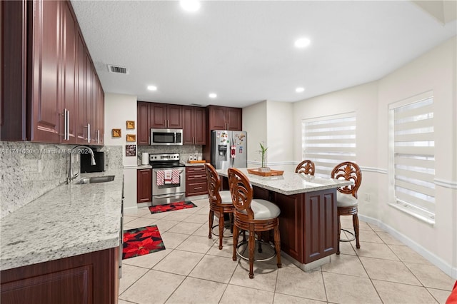 kitchen featuring backsplash, light stone counters, stainless steel appliances, sink, and a kitchen island