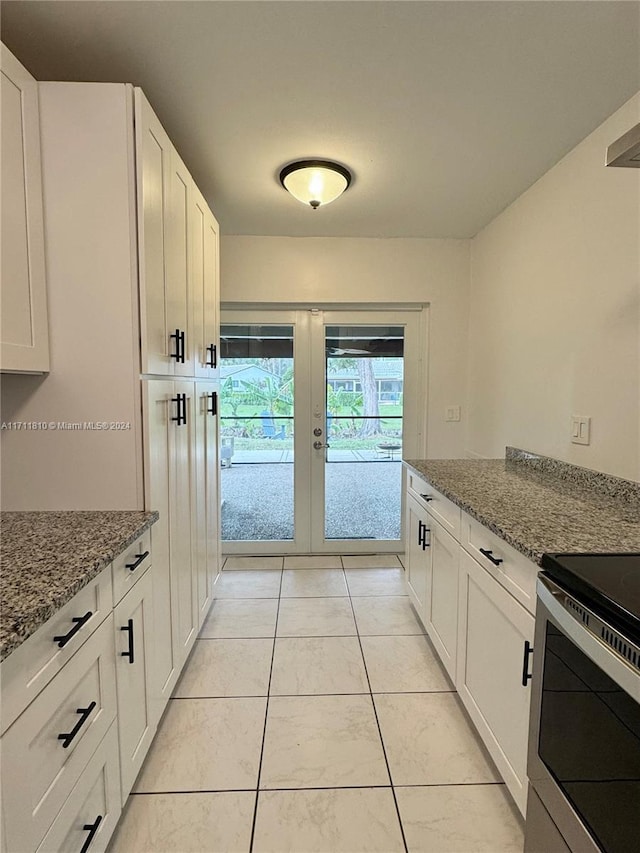 kitchen with stainless steel electric range, white cabinetry, light stone countertops, and light tile patterned floors