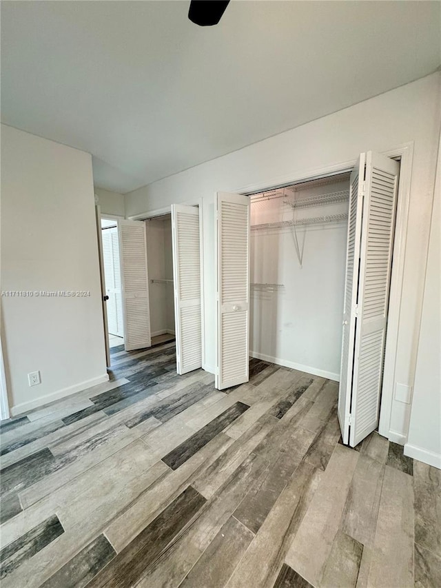 unfurnished bedroom featuring wood-type flooring and multiple closets