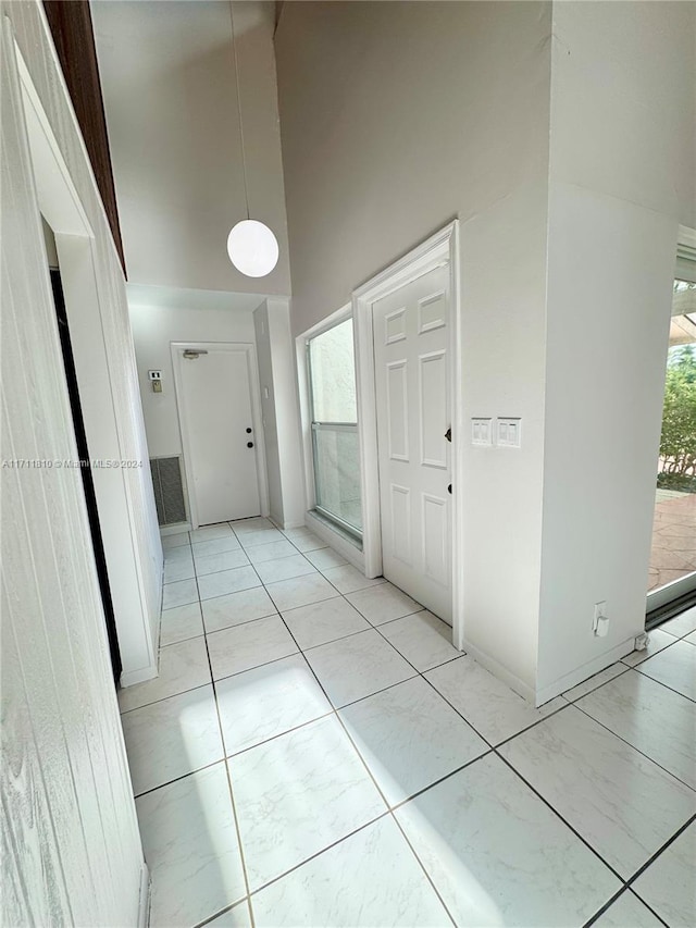 hallway with light tile patterned flooring, a healthy amount of sunlight, and a high ceiling