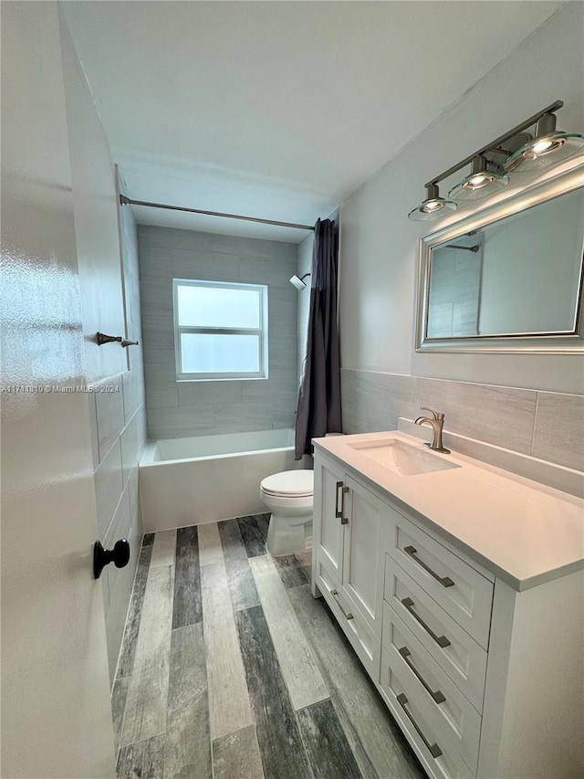 full bathroom featuring hardwood / wood-style floors, vanity, toilet, shower / bathtub combination with curtain, and tile walls