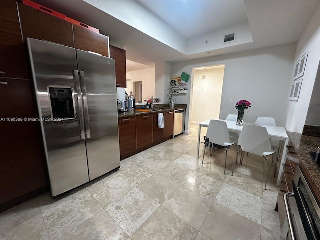 kitchen with a tray ceiling, dark stone counters, and appliances with stainless steel finishes