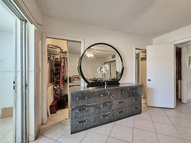 tiled bedroom featuring a walk in closet, a textured ceiling, and a closet