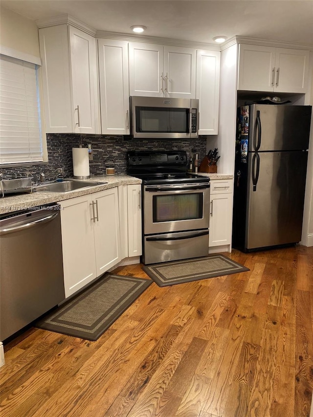 kitchen with white cabinetry, sink, stainless steel appliances, decorative backsplash, and light wood-type flooring