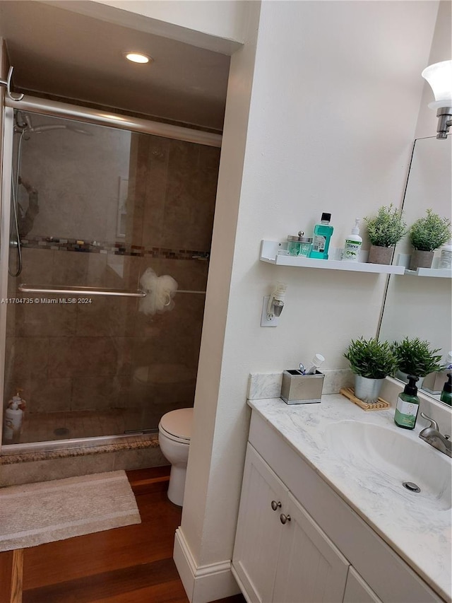 bathroom featuring vanity, toilet, wood-type flooring, and a shower with door