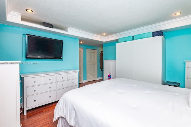 bedroom with a tray ceiling, crown molding, a textured ceiling, and hardwood / wood-style flooring