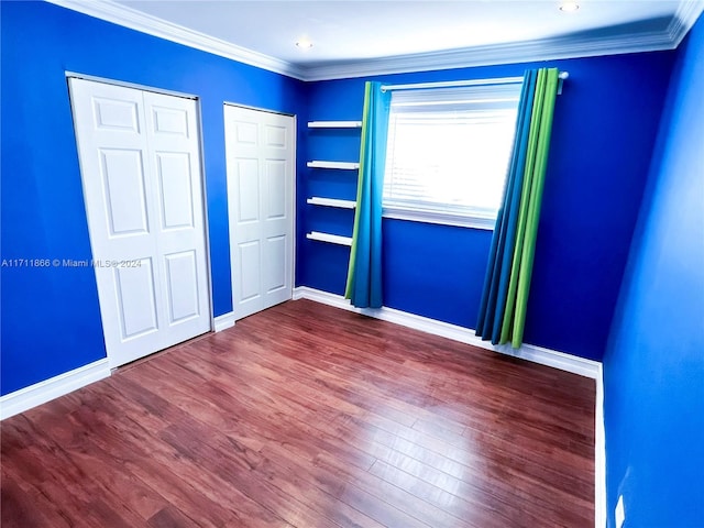 unfurnished bedroom with hardwood / wood-style flooring, ornamental molding, and multiple closets