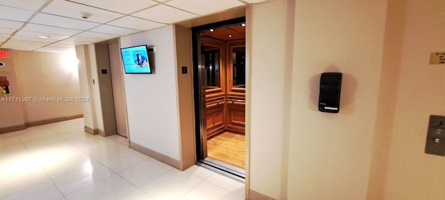 hall featuring a drop ceiling, light tile patterned flooring, and elevator