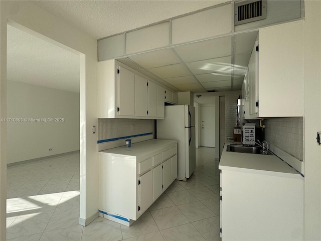 kitchen with a paneled ceiling, backsplash, white cabinets, sink, and white fridge