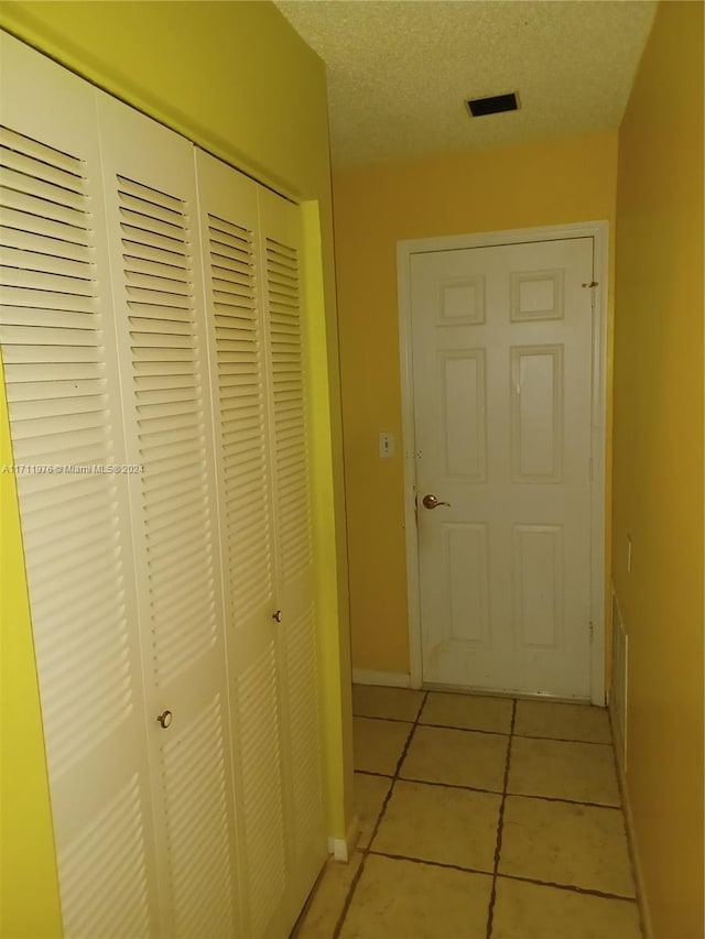 hallway with a textured ceiling and light tile patterned flooring