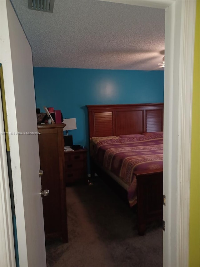 bedroom featuring dark colored carpet, a textured ceiling, and ceiling fan