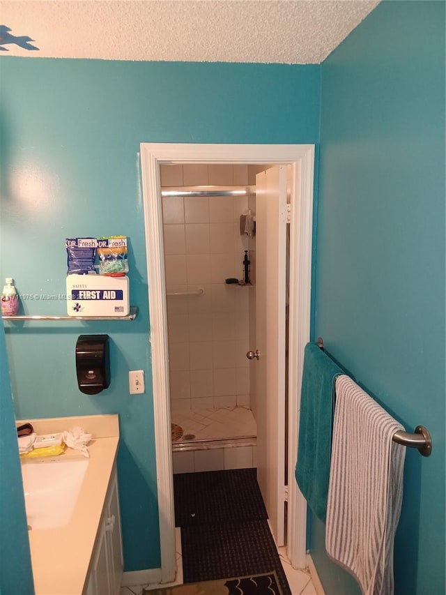 bathroom with tile patterned floors, vanity, a tile shower, and a textured ceiling