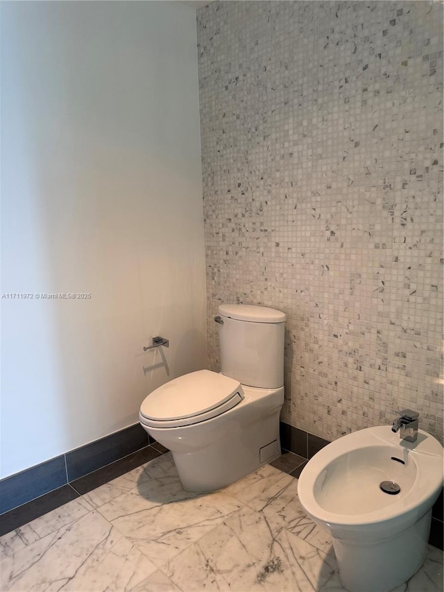 half bath featuring toilet, marble finish floor, baseboards, and a bidet