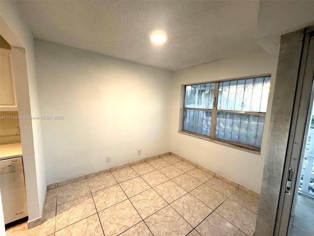 empty room with a textured ceiling, light tile patterned flooring, and baseboards