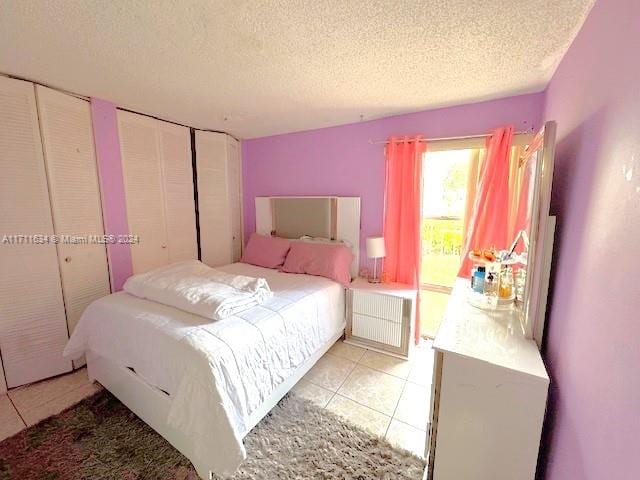 bedroom with multiple closets, radiator heating unit, light tile patterned floors, and a textured ceiling