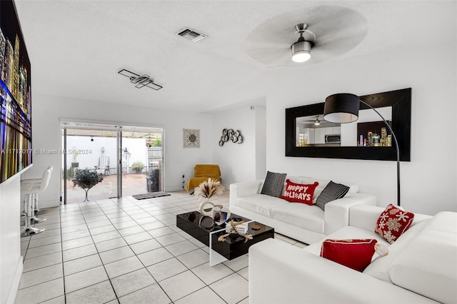 living room featuring ceiling fan, light tile patterned flooring, and a textured ceiling