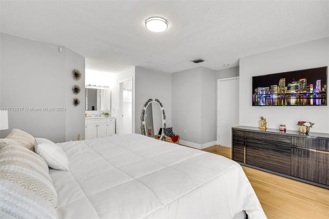 bedroom featuring a textured ceiling, connected bathroom, and light hardwood / wood-style floors