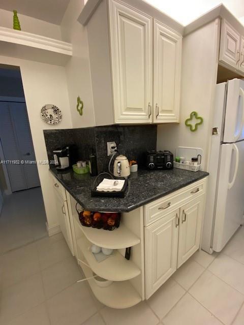 kitchen featuring white refrigerator, dark stone countertops, light tile patterned floors, and backsplash