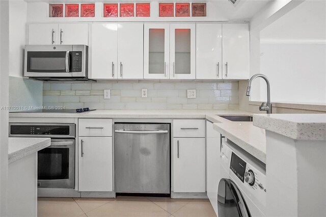 kitchen with stainless steel appliances, sink, light tile patterned floors, white cabinets, and washer / clothes dryer