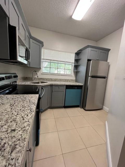 kitchen featuring light stone countertops, light tile patterned floors, stainless steel appliances, and gray cabinets