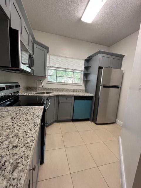 kitchen with sink, light tile patterned floors, appliances with stainless steel finishes, light stone countertops, and a textured ceiling