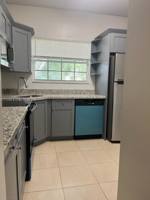 kitchen featuring sink, light tile patterned floors, stainless steel appliances, light stone counters, and a healthy amount of sunlight