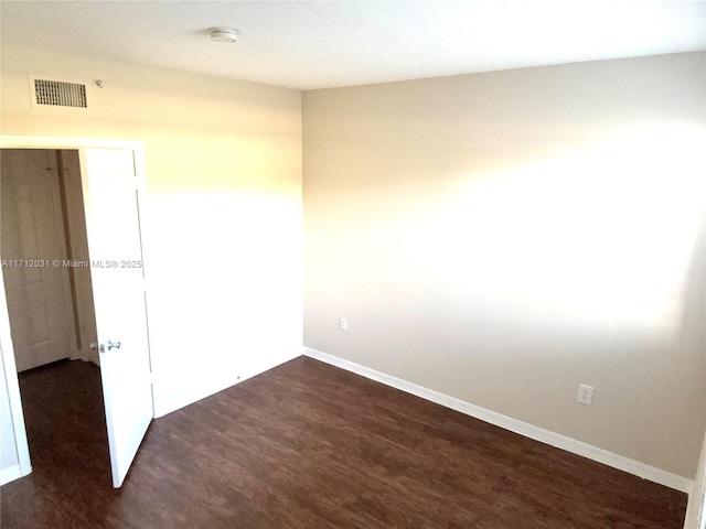 empty room featuring dark wood finished floors, visible vents, and baseboards