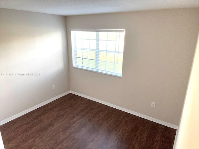 unfurnished room with baseboards and dark wood-type flooring