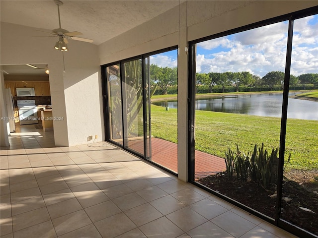 unfurnished sunroom with ceiling fan, a water view, and a healthy amount of sunlight