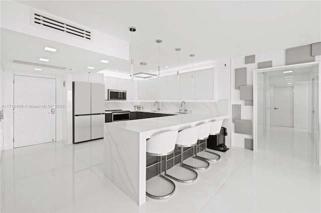 kitchen featuring white cabinetry, light stone countertops, pendant lighting, a kitchen bar, and appliances with stainless steel finishes